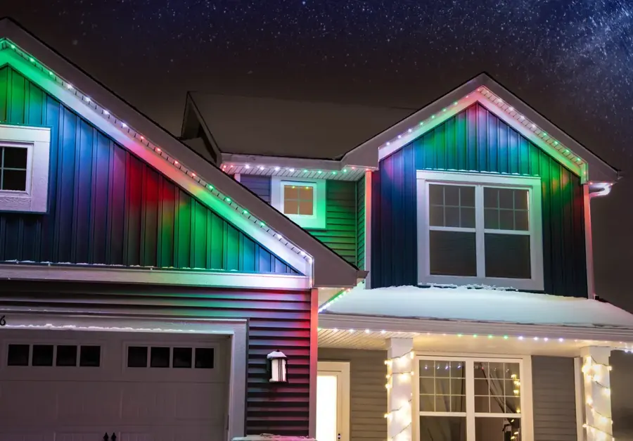 Two story Capital Region home with multi color permanent roofline lighting on a snowy night